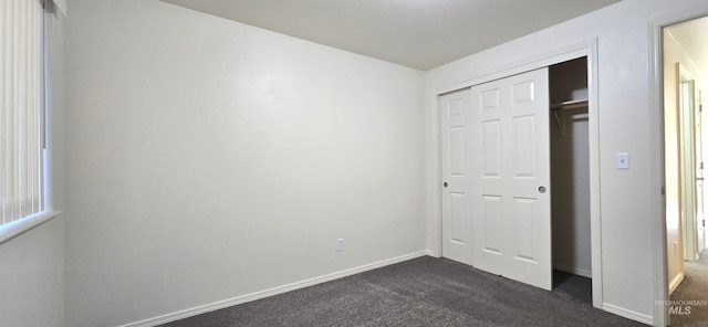 unfurnished bedroom featuring dark colored carpet, a closet, and baseboards