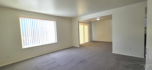 spare room featuring dark carpet and baseboards