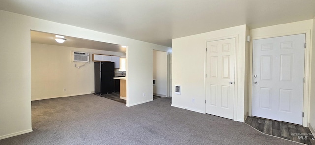 unfurnished bedroom with a wall unit AC, visible vents, baseboards, freestanding refrigerator, and dark colored carpet