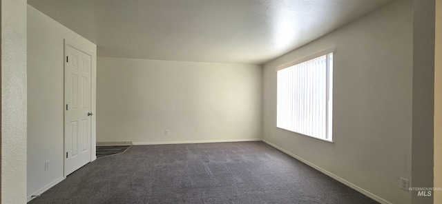 spare room featuring dark colored carpet, plenty of natural light, and baseboards