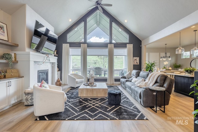 living area with a premium fireplace, light wood-style floors, high vaulted ceiling, and ceiling fan