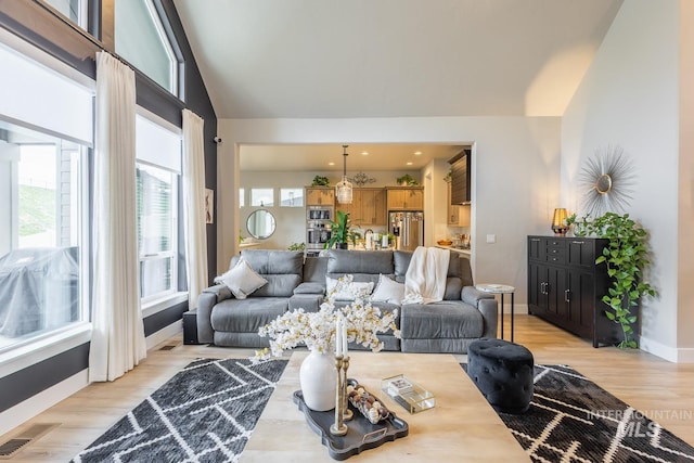 living area featuring baseboards, vaulted ceiling, visible vents, and light wood-style floors