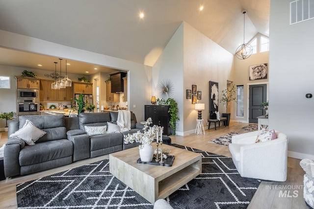 living area with high vaulted ceiling, plenty of natural light, an inviting chandelier, light wood-style flooring, and visible vents