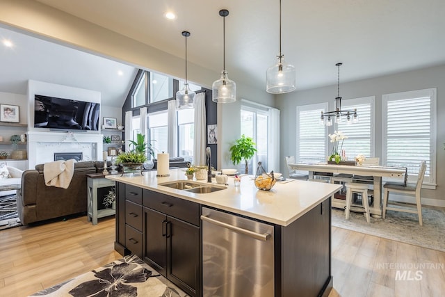 kitchen featuring stainless steel dishwasher, a sink, light wood-style floors, light countertops, and a fireplace