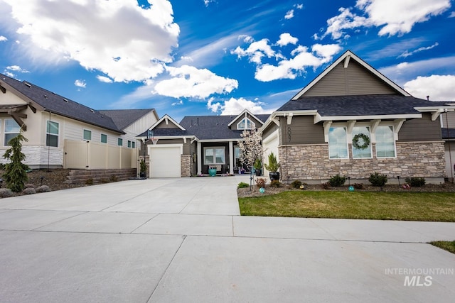 view of front facade with concrete driveway, a front lawn, stone siding, a garage, and roof with shingles