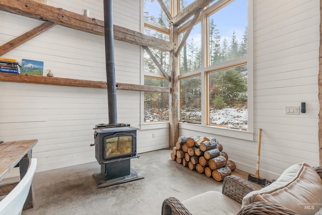 living room featuring wood walls, a wood stove, a high ceiling, and concrete flooring