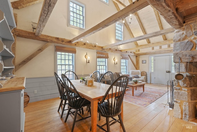 dining space with beam ceiling, light hardwood / wood-style floors, and high vaulted ceiling