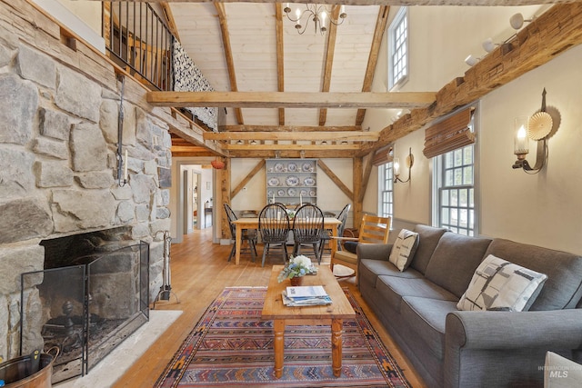 living room featuring high vaulted ceiling, a stone fireplace, light wood-type flooring, beamed ceiling, and wood ceiling