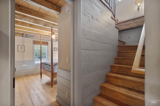 staircase with beam ceiling, wooden walls, hardwood / wood-style floors, and wood ceiling