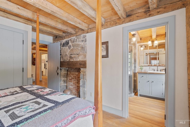 bedroom with wooden ceiling, sink, light wood-type flooring, connected bathroom, and beam ceiling