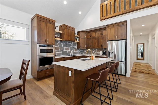 kitchen featuring light stone countertops, stainless steel appliances, a kitchen island with sink, sink, and light hardwood / wood-style floors