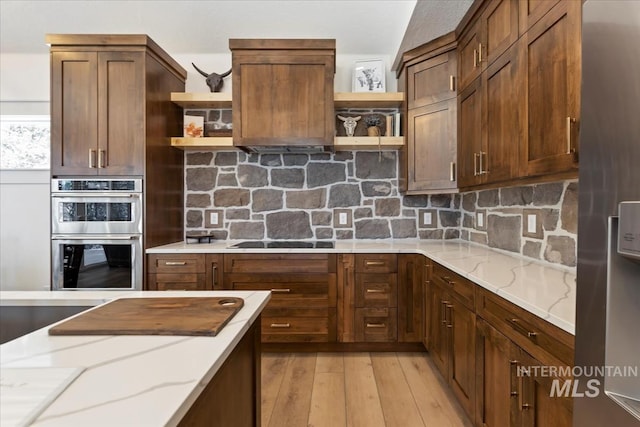 kitchen with light stone countertops, backsplash, stainless steel appliances, and light hardwood / wood-style flooring