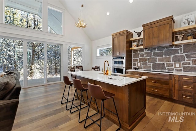 kitchen with high vaulted ceiling, a kitchen breakfast bar, black stovetop, hardwood / wood-style flooring, and an island with sink