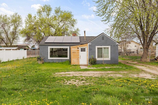 view of front of house featuring a shingled roof, solar panels, stucco siding, a front lawn, and fence private yard