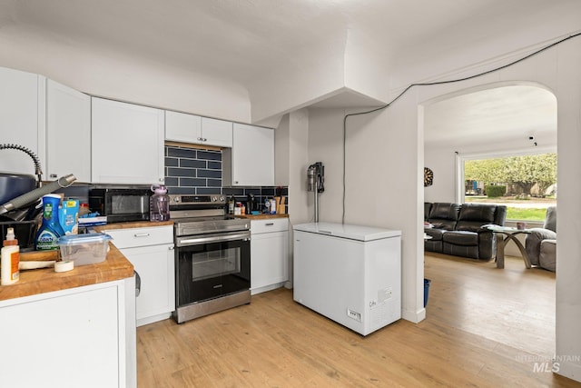 kitchen featuring white cabinets, arched walkways, refrigerator, and electric range