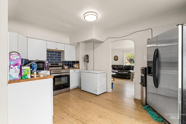 kitchen with arched walkways, appliances with stainless steel finishes, white cabinetry, light wood-style flooring, and decorative backsplash