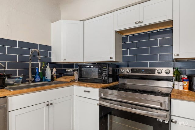 kitchen with white cabinets, appliances with stainless steel finishes, a sink, butcher block countertops, and backsplash