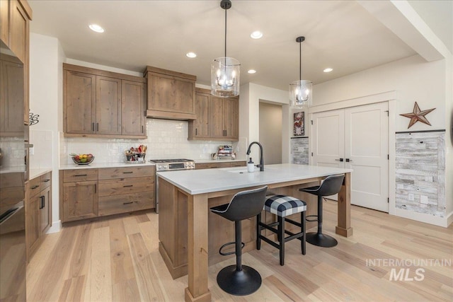 kitchen featuring a center island with sink, gas range, pendant lighting, sink, and a kitchen bar