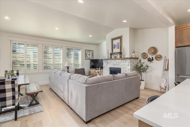 living room featuring light hardwood / wood-style flooring, a stone fireplace, and vaulted ceiling