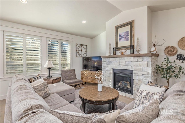 living room with hardwood / wood-style floors, lofted ceiling, and a stone fireplace