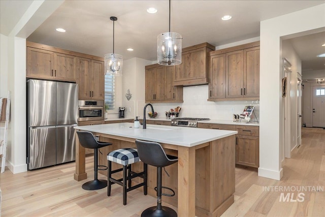 kitchen featuring light hardwood / wood-style flooring, backsplash, pendant lighting, stainless steel appliances, and an island with sink