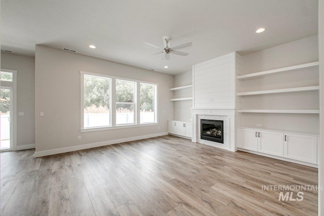 unfurnished living room with built in shelves, ceiling fan, a high end fireplace, and light hardwood / wood-style flooring