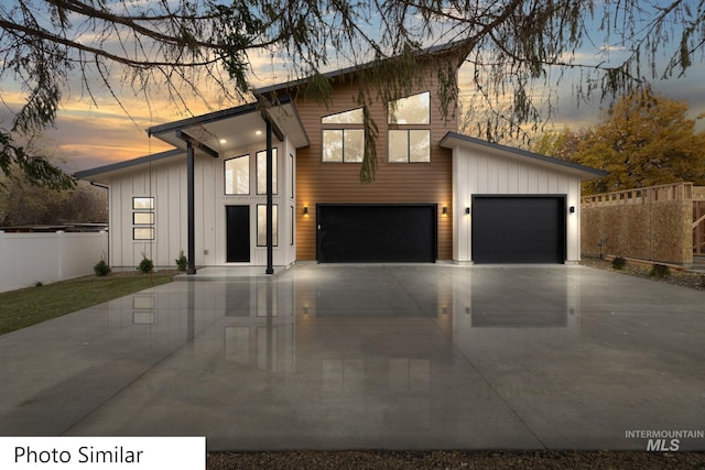 contemporary house featuring a garage, board and batten siding, driveway, and fence