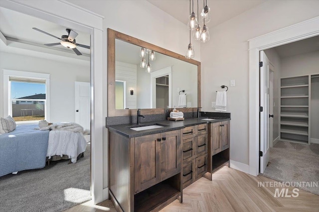 full bathroom with double vanity, connected bathroom, baseboards, and a sink