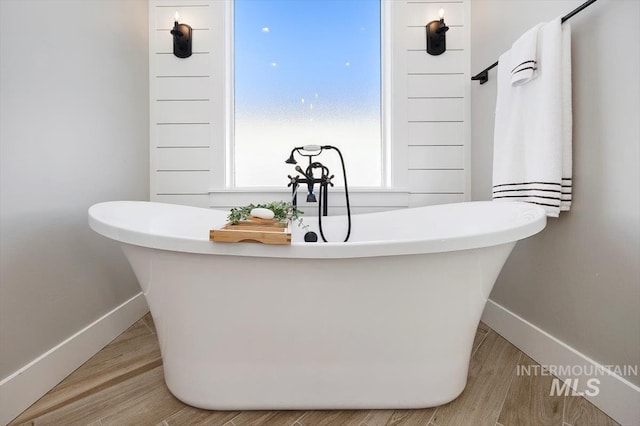 full bath featuring a soaking tub, baseboards, and wood finished floors