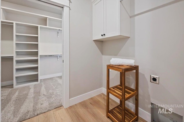 laundry room featuring light wood-type flooring, cabinet space, electric dryer hookup, and baseboards