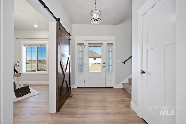 foyer entrance with light wood-type flooring, a wealth of natural light, stairway, and a barn door