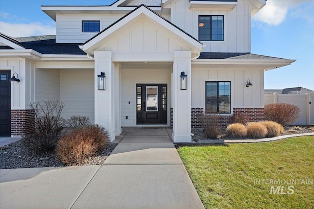 doorway to property with board and batten siding, brick siding, a porch, and roof with shingles