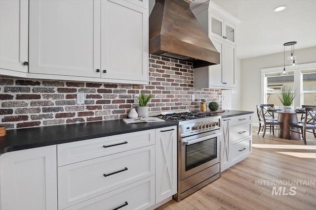 kitchen featuring dark countertops, custom range hood, decorative backsplash, white cabinets, and high end stove