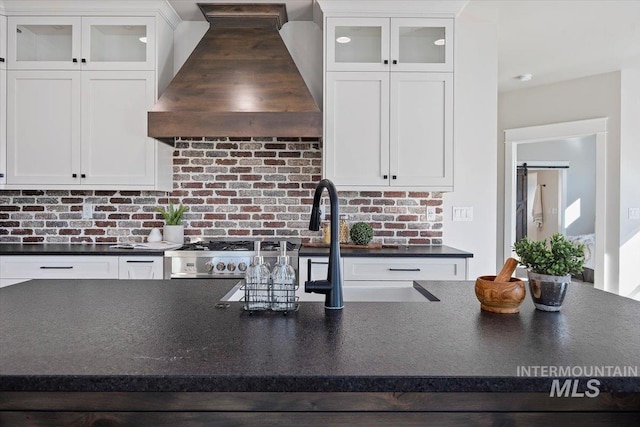 kitchen with premium range hood, dark countertops, glass insert cabinets, and white cabinets