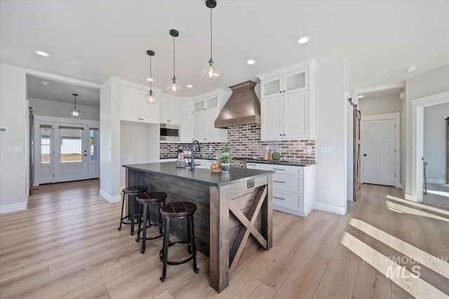 kitchen featuring tasteful backsplash, dark countertops, stainless steel microwave, a barn door, and premium range hood