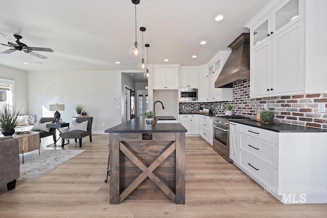 kitchen with premium range hood, a sink, open floor plan, appliances with stainless steel finishes, and dark countertops