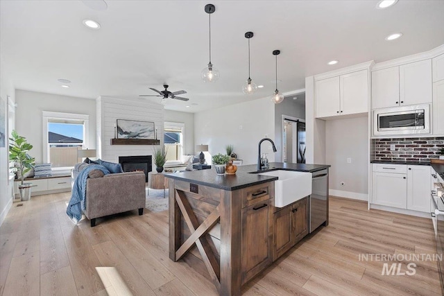 kitchen with a fireplace, stainless steel appliances, dark countertops, light wood-style flooring, and a healthy amount of sunlight