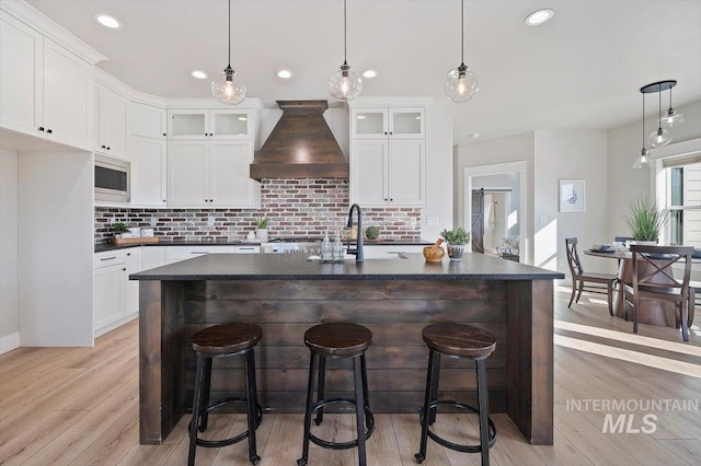 kitchen featuring a sink, stainless steel microwave, dark countertops, and custom exhaust hood