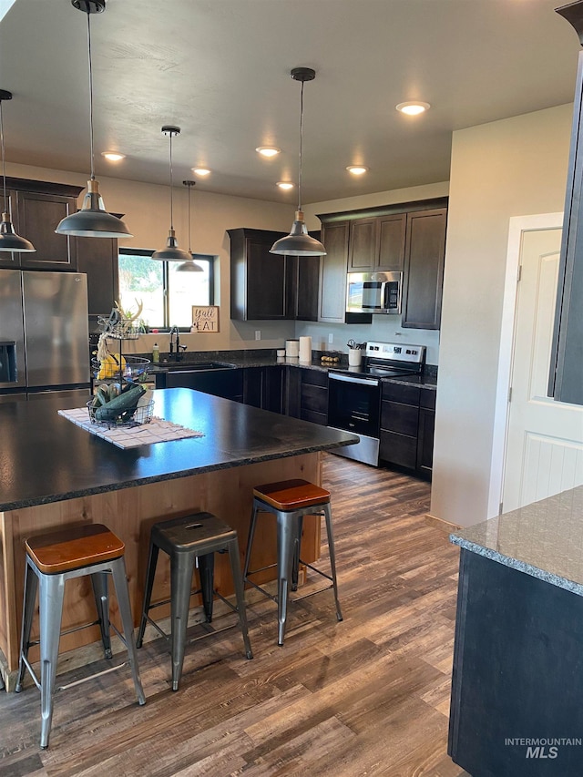 kitchen featuring dark wood-type flooring, hanging light fixtures, stainless steel appliances, and a breakfast bar