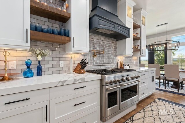 kitchen with white cabinetry, backsplash, premium range hood, light hardwood / wood-style floors, and range with two ovens