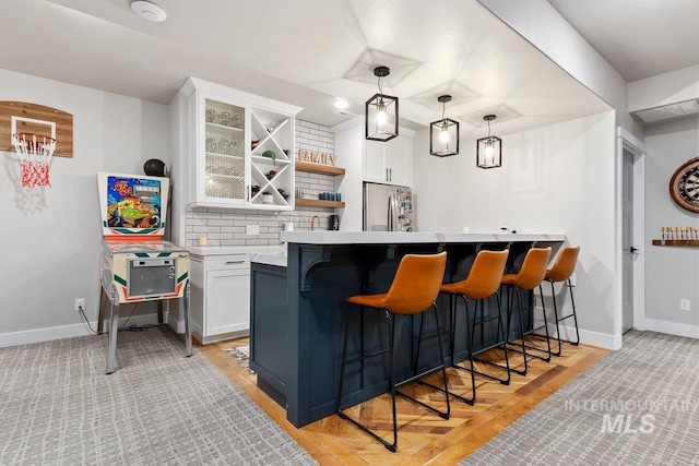 bar featuring white cabinets, stainless steel fridge, decorative backsplash, and hanging light fixtures