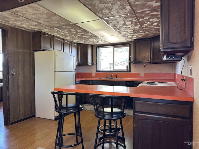 kitchen featuring sink, white appliances, dark brown cabinets, a kitchen breakfast bar, and light hardwood / wood-style floors