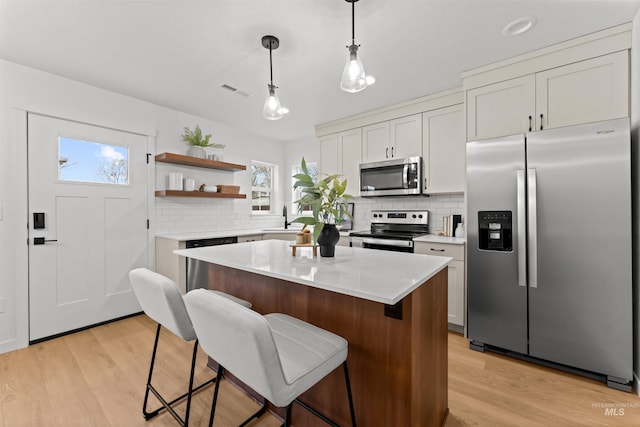 kitchen featuring hanging light fixtures, tasteful backsplash, a kitchen island, white cabinetry, and stainless steel appliances