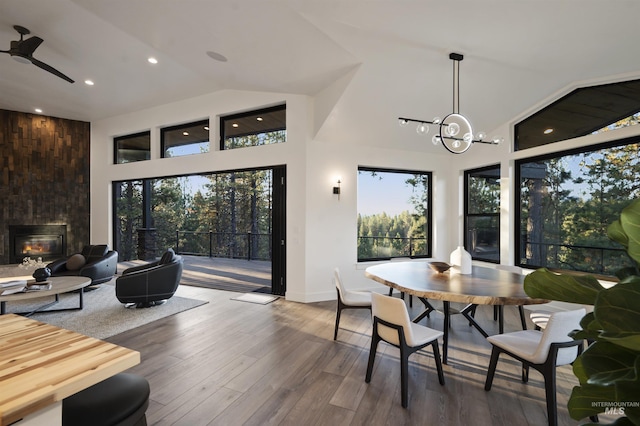 dining space featuring a healthy amount of sunlight, a fireplace, high vaulted ceiling, and wood finished floors