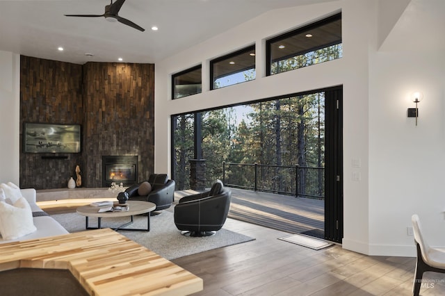 living room with ceiling fan, a towering ceiling, a large fireplace, recessed lighting, and wood finished floors