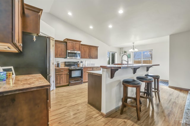 kitchen featuring light wood finished floors, stainless steel microwave, a kitchen bar, an inviting chandelier, and electric range