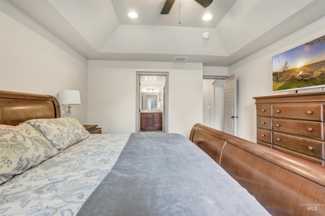 bedroom with visible vents, ceiling fan, ensuite bath, and a tray ceiling