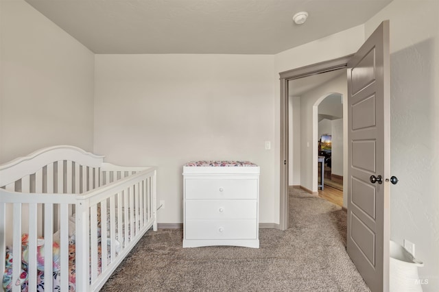 carpeted bedroom featuring a nursery area, baseboards, and arched walkways