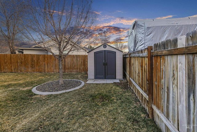 yard at dusk featuring an outbuilding, a storage unit, and a fenced backyard