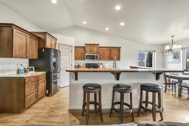 kitchen featuring a kitchen breakfast bar, stainless steel appliances, an inviting chandelier, light wood finished floors, and vaulted ceiling